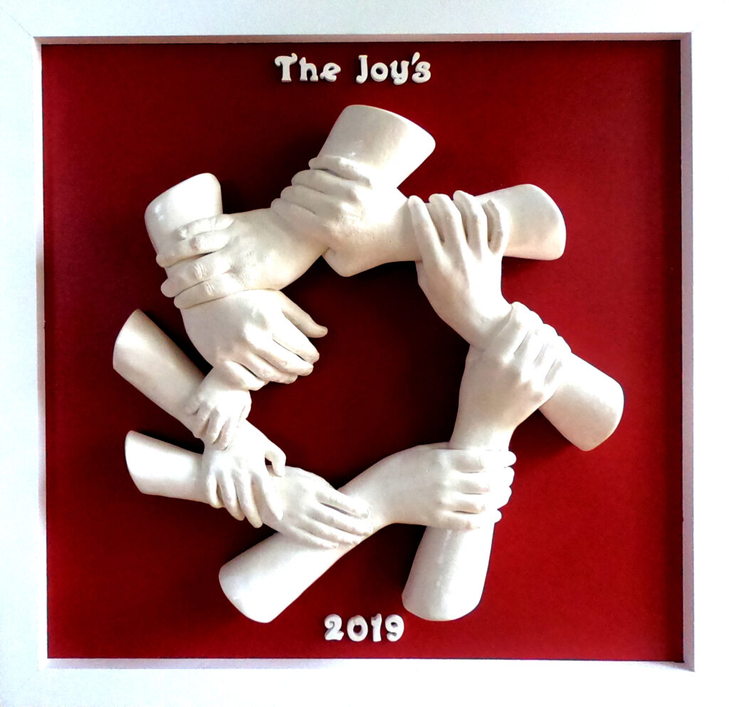 The joys White sculpted hands and forearms interlock in a circular chain against a deep red background, with the words “The Joy’s” above and “2019” below